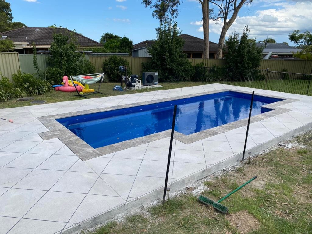 Suburban backyard swimming pool with tiled surround and lawn