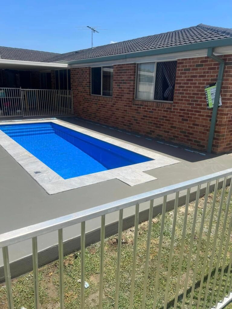 Backyard swimming pool beside brick house with fence