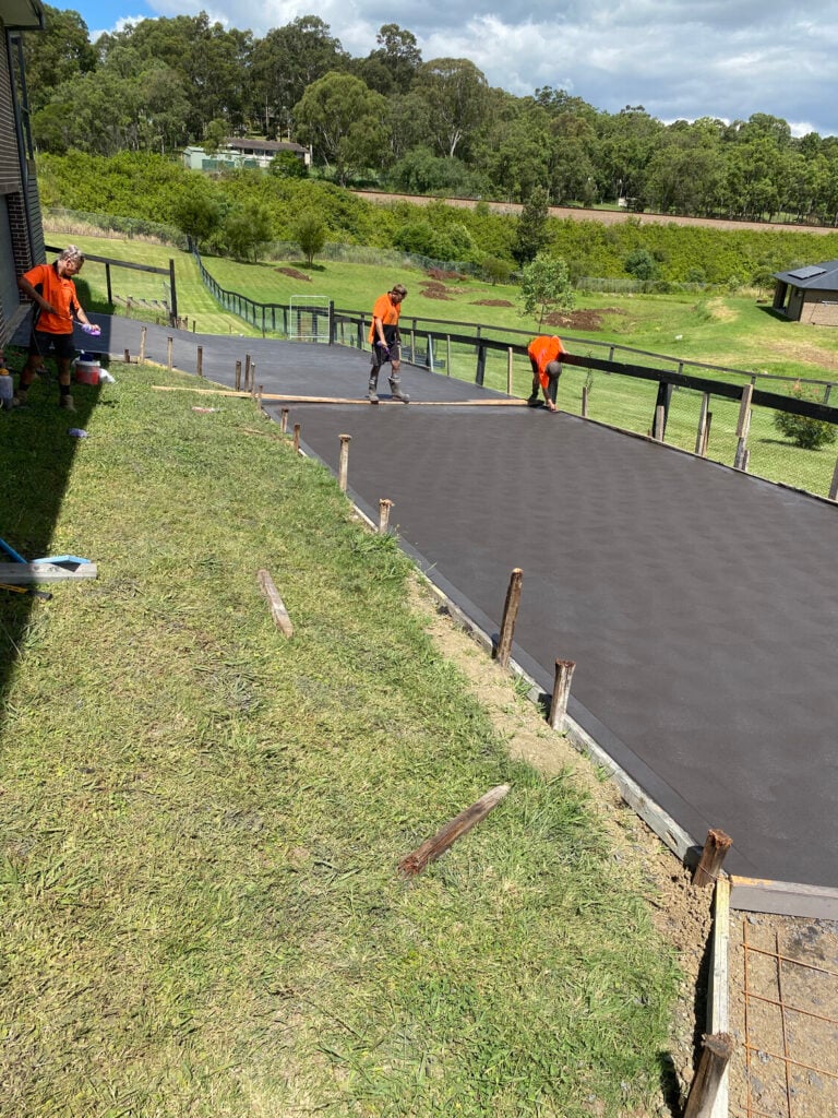 Workers smoothing freshly poured concrete pathway outdoors