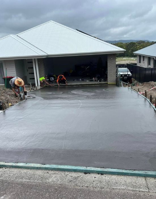 Workers smoothing freshly poured concrete driveway outside house