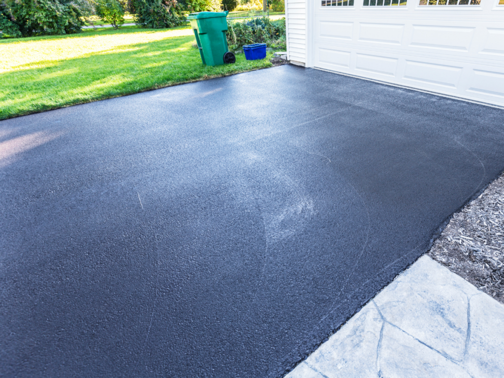 Freshly sealed asphalt driveway beside suburban garage