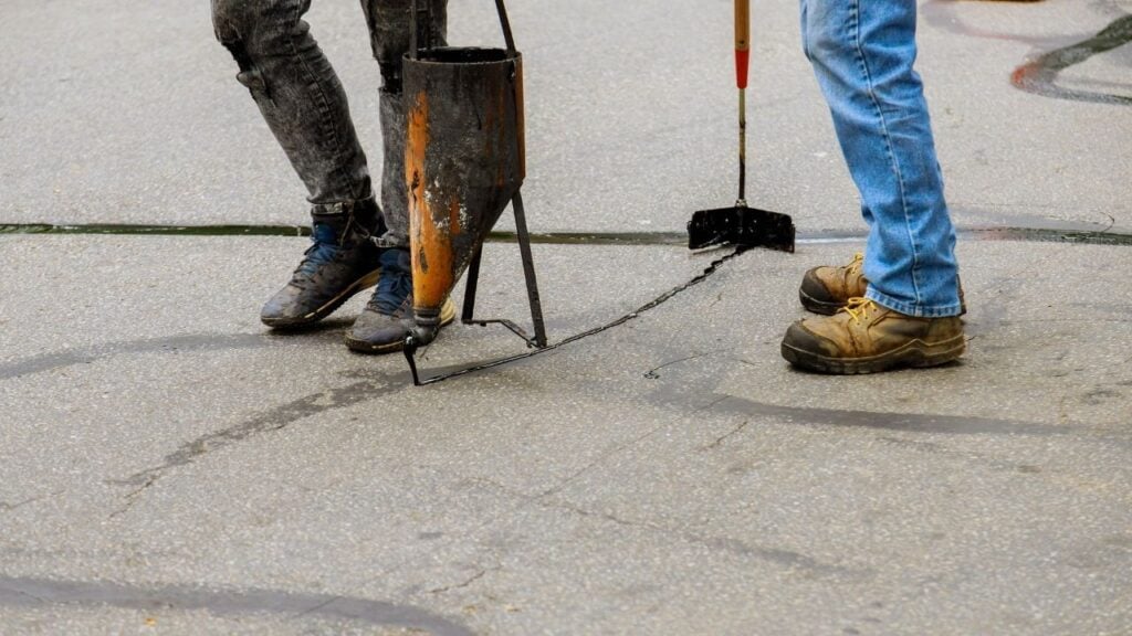 apply black sealant into cracks on a grey paved surface