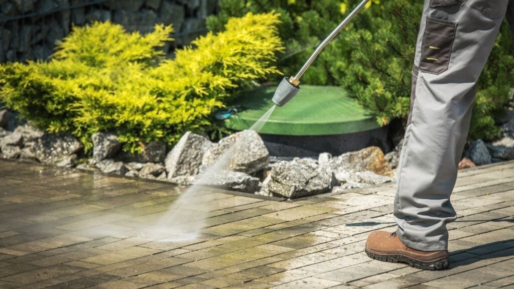 A pressure washer wand sprays a strong jet of water onto outdoor paving, effectively cleaning the surface.
