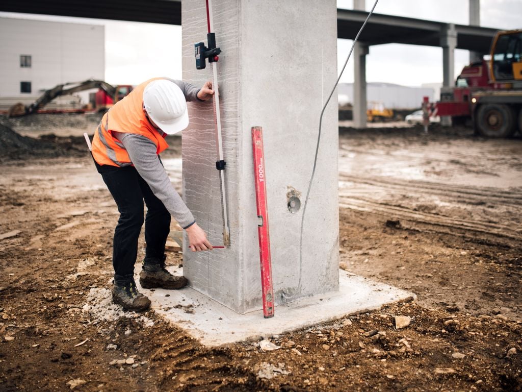 Construction worker measuring concrete column with spirit level