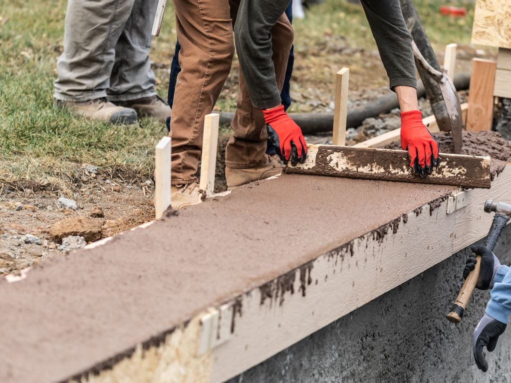 Workers smoothing wet concrete in timber formwork