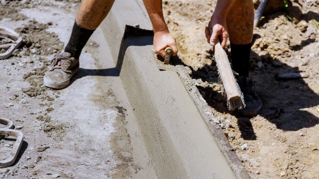 Worker smoothing fresh concrete curb with trowel