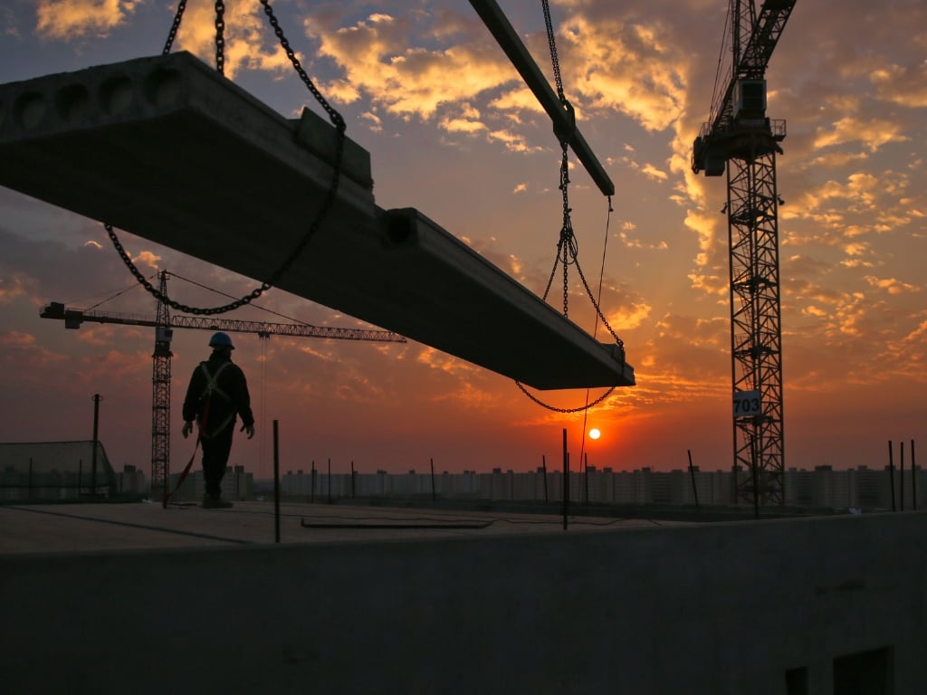 Construction worker and crane lifting beam at sunset