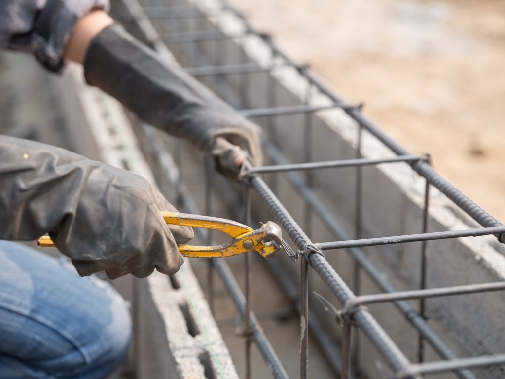 Worker tying steel reinforcement bars with pliers before concrete pour