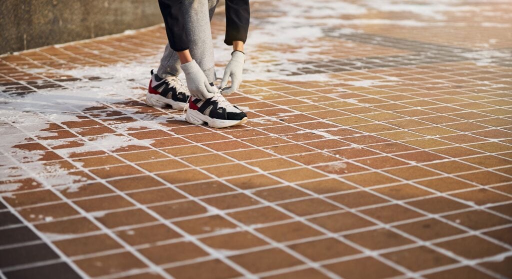 Person tying running shoes on frosty pavement