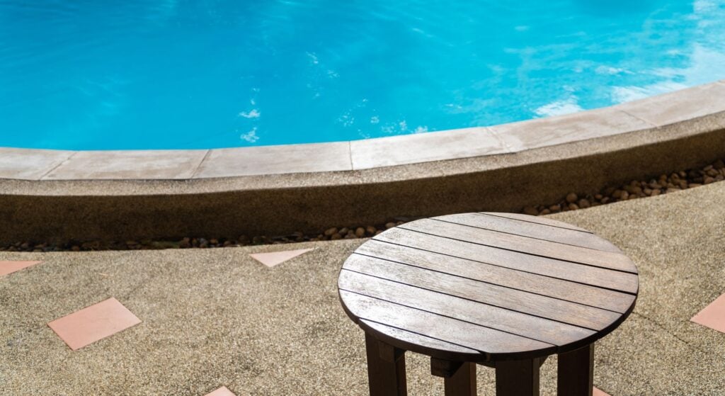 Round wooden table beside backyard swimming pool