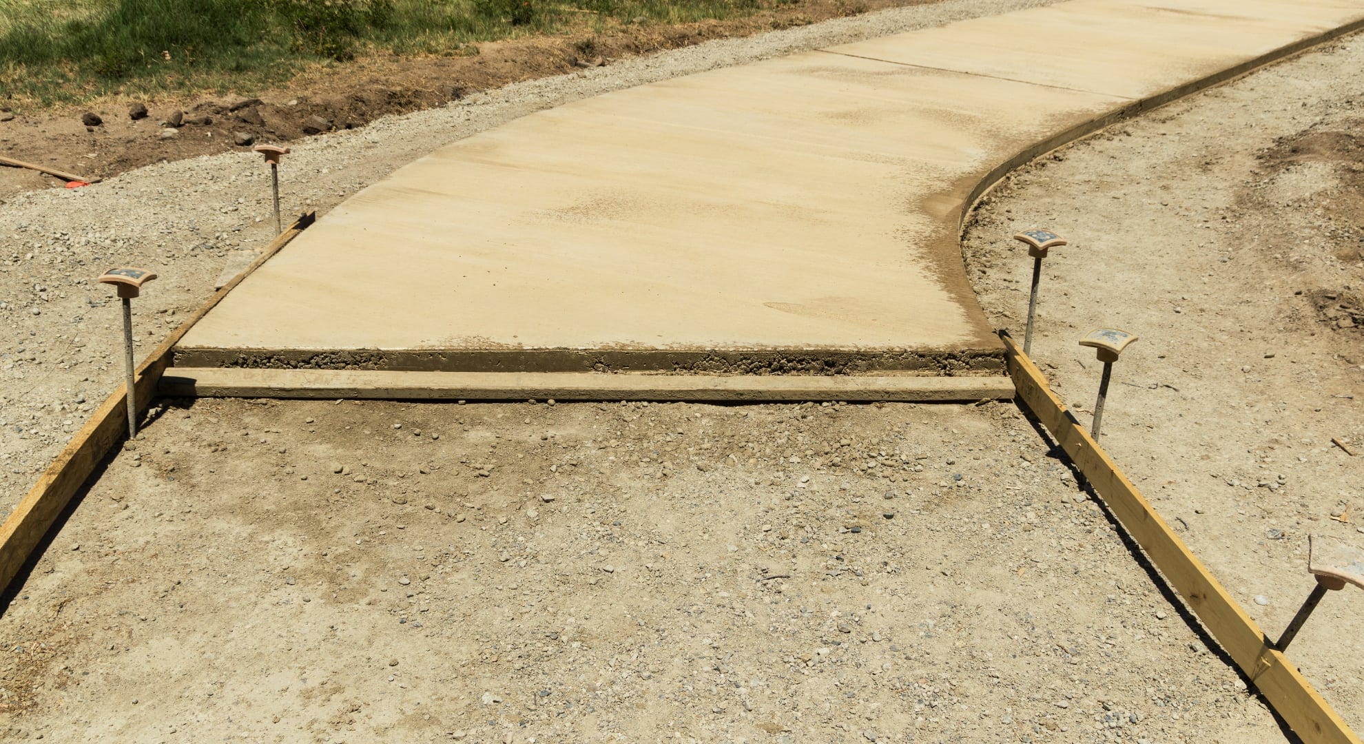 A concrete walkway under construction, showing the wet concrete, metal edging, and gravel base.