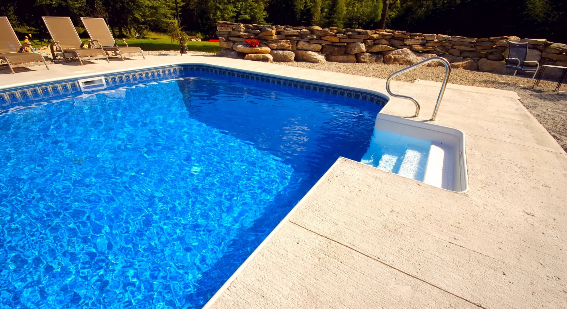 A backyard oasis featuring a sparkling blue pool, a stone patio, and a metal pool ladder
