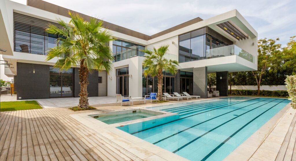 A luxurious modern house with a spacious pool area and palm trees, featuring large windows and a sleek design