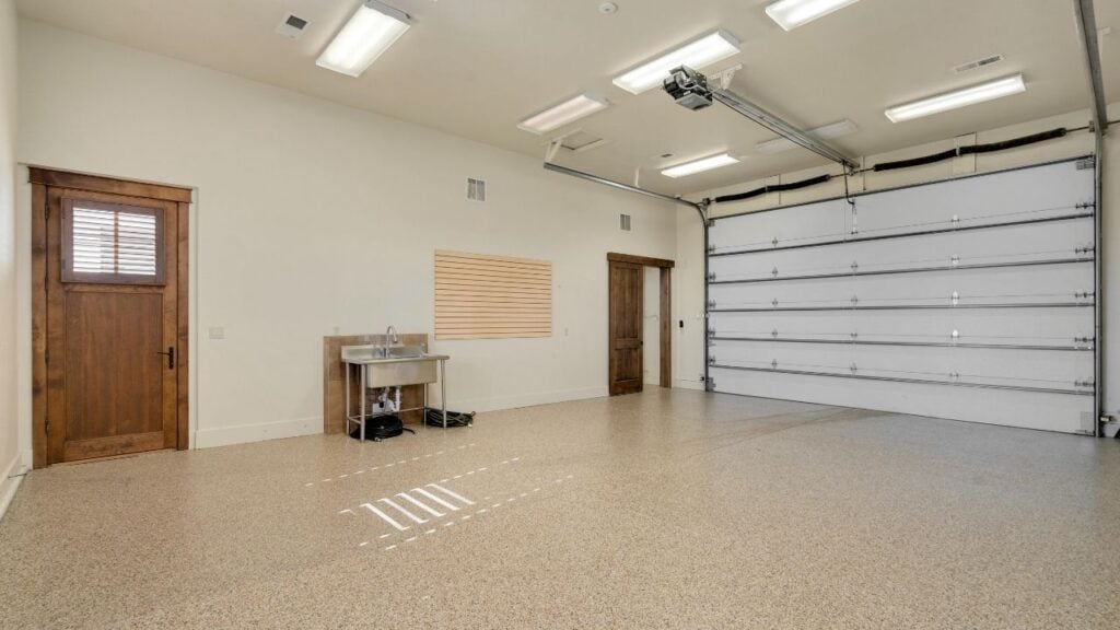 An empty, well-lit garage showcasing a recently sealed floor that gleams with a speckled finish, indicating an epoxy or similar coating. 