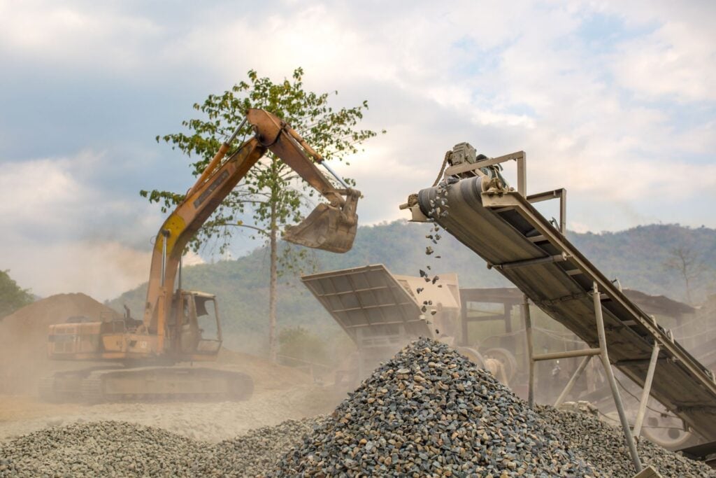 Excavator and conveyor moving gravel at quarry site