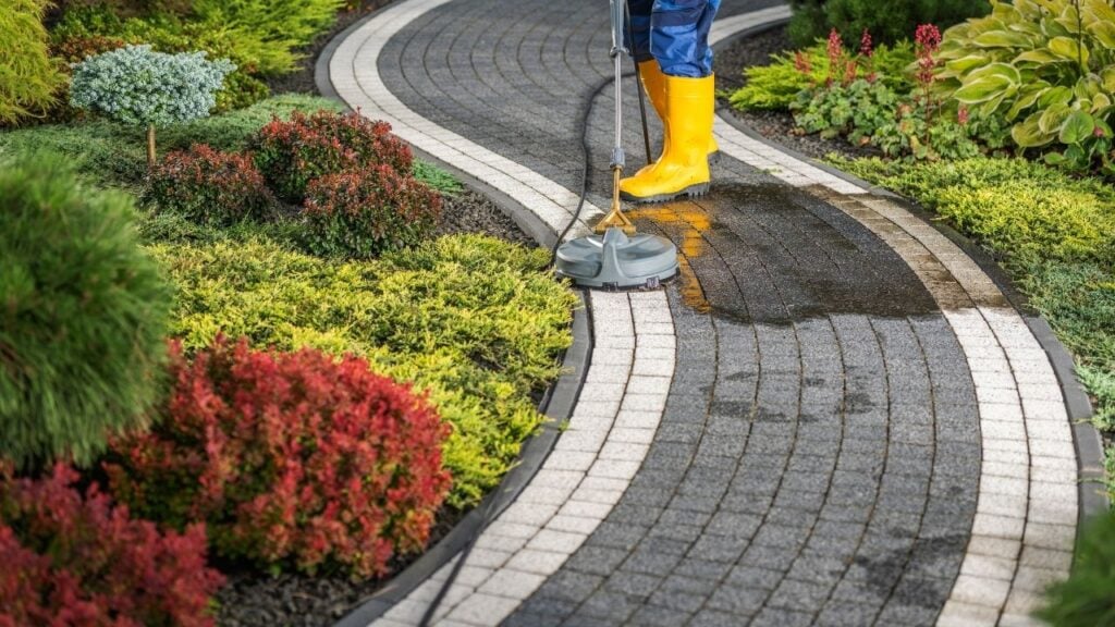 Person pressure washing curved garden pathway in backyard