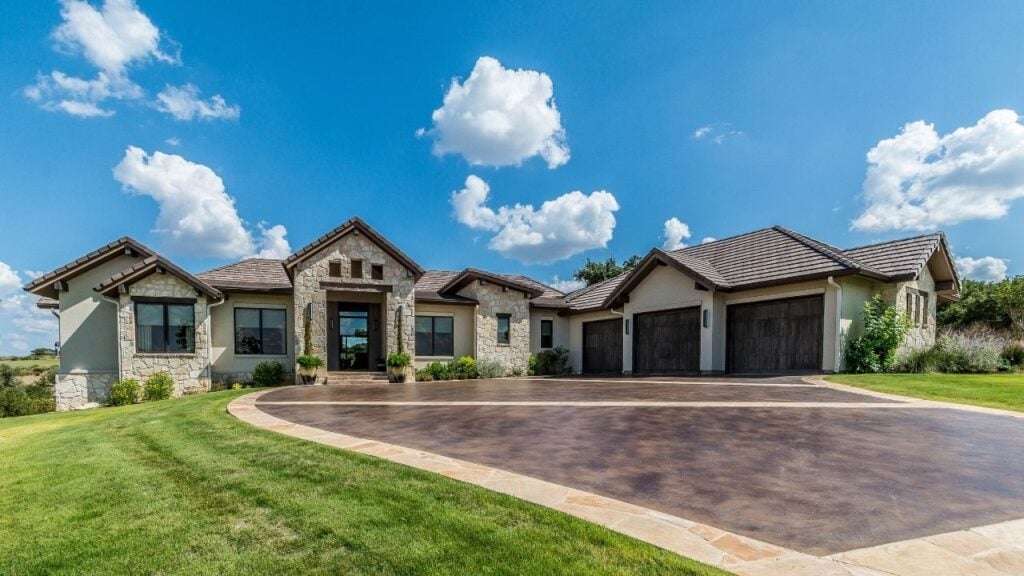 In the foreground, a expansive, dark brown stamped concrete driveway with a subtle sheen, characteristic of a protective matte sealer, curves elegantly towards the house and garage.