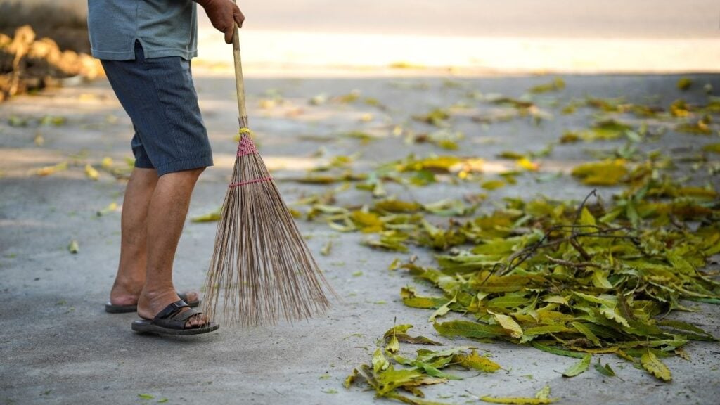 Worker sweeping dry leaves off concrete patio before pressure washing