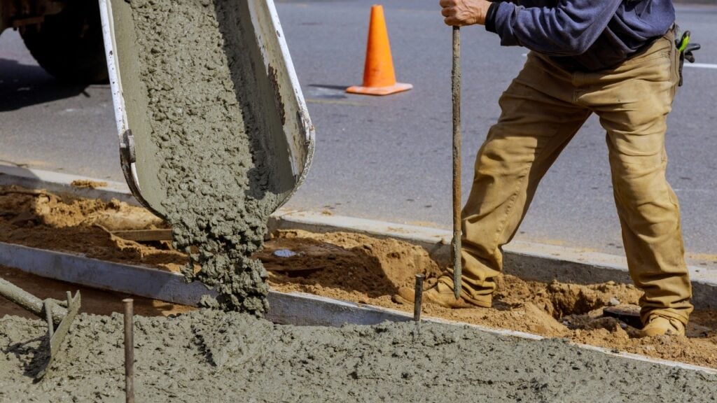 Worker pouring concrete into roadside kerb formwork