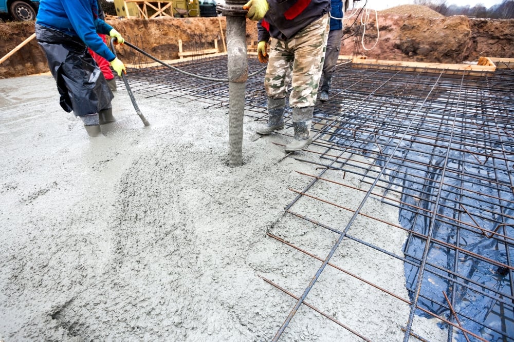 Workers pouring concrete over steel reinforcement mesh