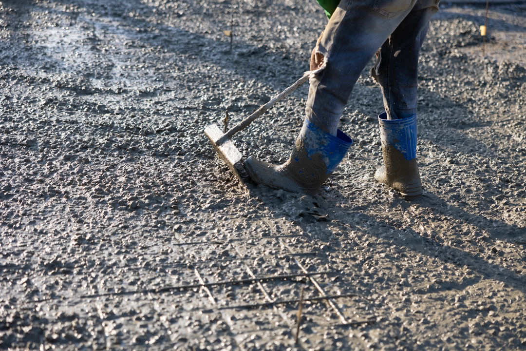 Worker smoothing wet concrete with rake tool