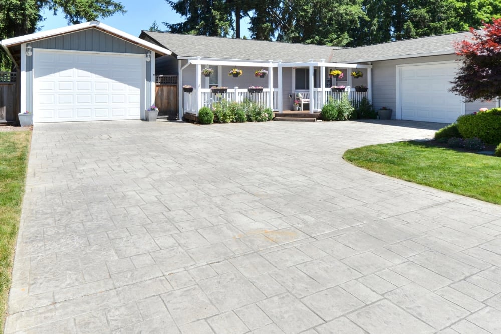 A large, wide stamped concrete driveway leading to a suburban house with two white garages.