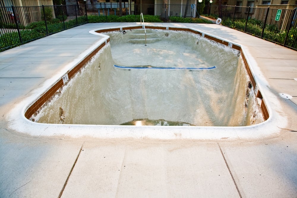 An empty concrete swimming pool shell undergoing installation, surrounded by a paved deck.