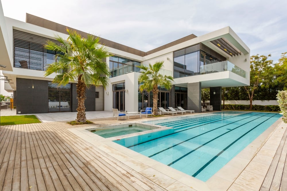 A luxurious, multi-story modern villa overlooking a long lap pool and attached spa.