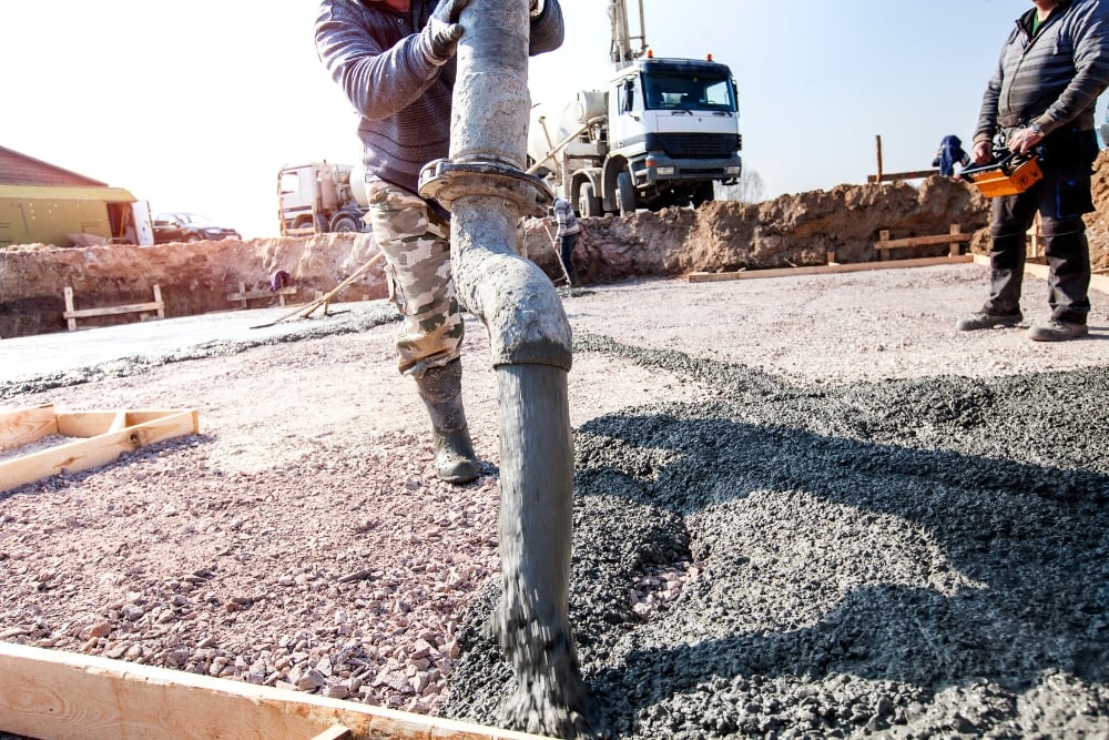 Construction worker pouring wet concrete from a pump hose onto a foundation slab.