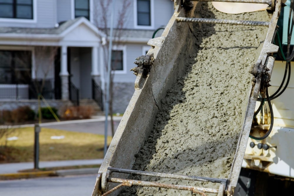 Close-up of wet concrete sliding down a cement truck chute outside a house.