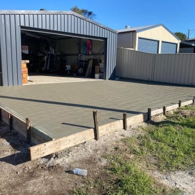 Freshly poured concrete slab beside metal garage shed