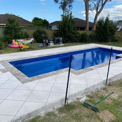 Suburban backyard swimming pool with tiled surround and lawn