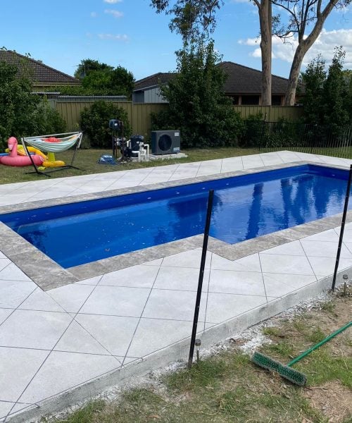 Suburban backyard swimming pool with tiled surround and lawn