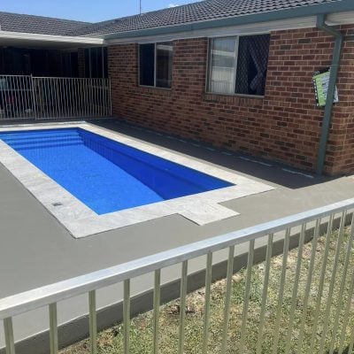 Backyard swimming pool beside brick house with fence