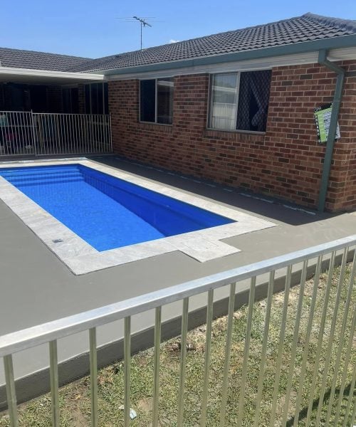 Backyard swimming pool beside brick house with fence