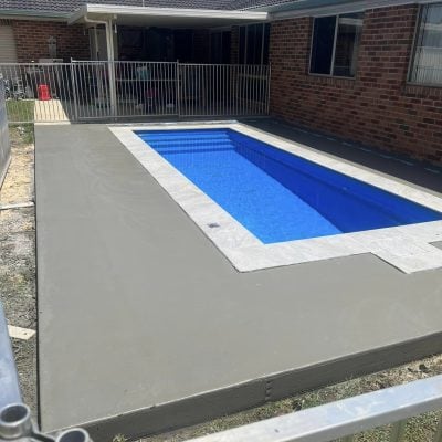 Backyard swimming pool with concrete surround and brick house