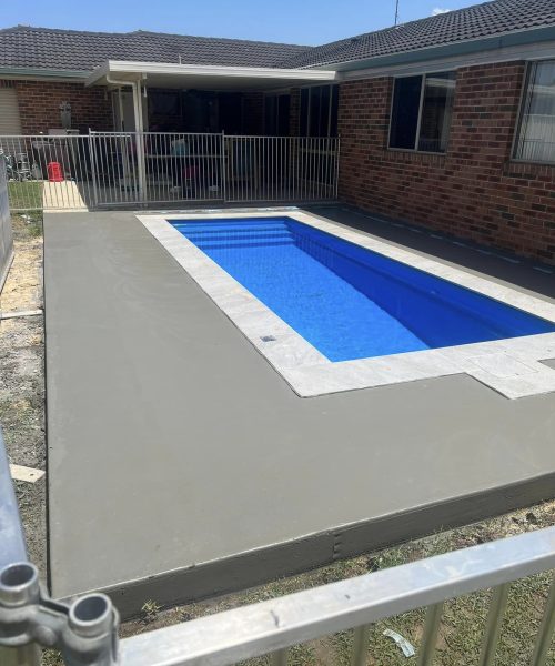 Backyard swimming pool with concrete surround and brick house