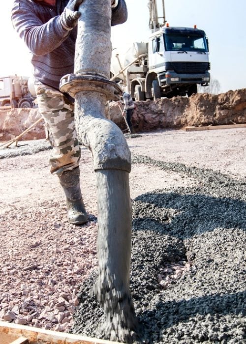 Construction worker pouring wet concrete from a pump hose onto a foundation slab.