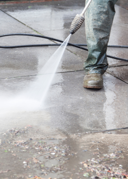 Worker pressure washing concrete pavement outdoors