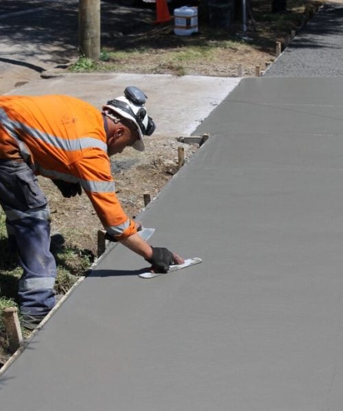 Construction worker smoothing fresh concrete footpath